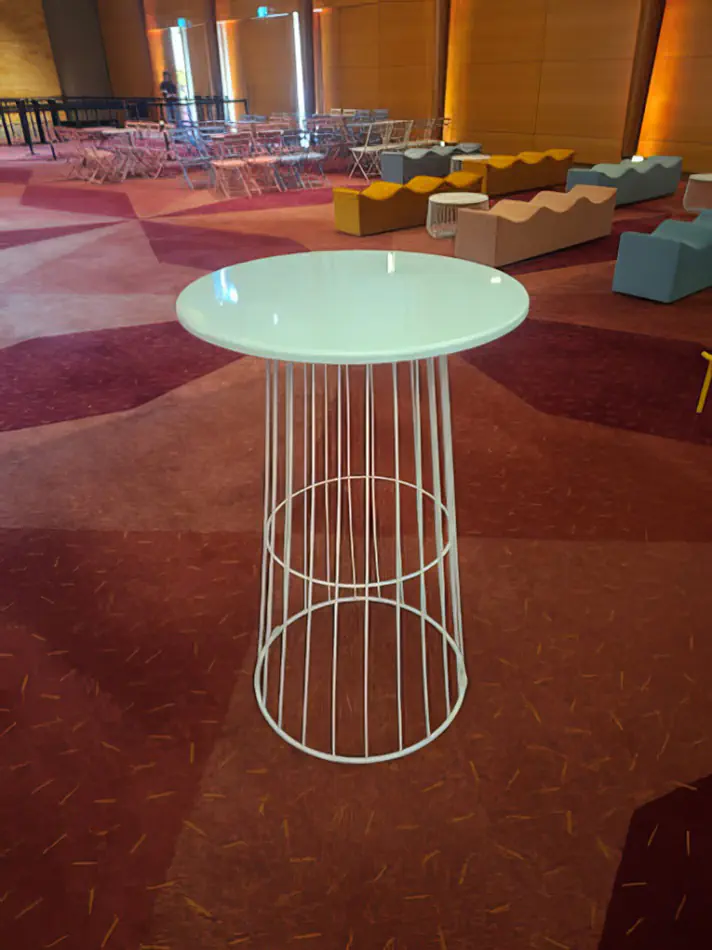 White wire cocktail table hire displayed in an indoor event venue with patterned carpet, lounge seating and ambient lighting in the background