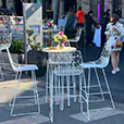 White wire cocktail table with matching bar stools set up outdoors at an event space with floral centrepiece and casual bar seating arrangement