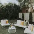 A white outdoor furniture set, including a white wire coffee table, in a backyard.