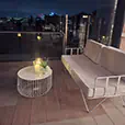 White wire coffee table with candle styling and white lounge seating arranged on a balcony event space overlooking the Sydney skyline at night