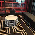 White wire coffee table paired with black velvet ottoman seating inside a modern event lounge with geometric patterned carpet and red lighting