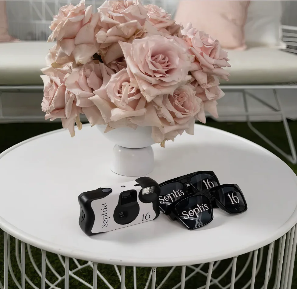 A white wire coffee table with a camera and a vase of roses.