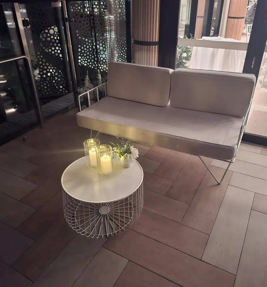 White wire lounge sofa with matching white wire coffee table, candles and floral styling arranged inside an elegant indoor event venue with timber flooring