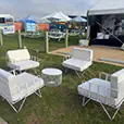 White wire lounge chairs with matching cushions and round wire coffee table styled on grass beside an outdoor marquee event setup