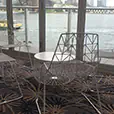White wire lounge chairs and matching round coffee table positioned indoors beside large windows overlooking a waterfront harbour view