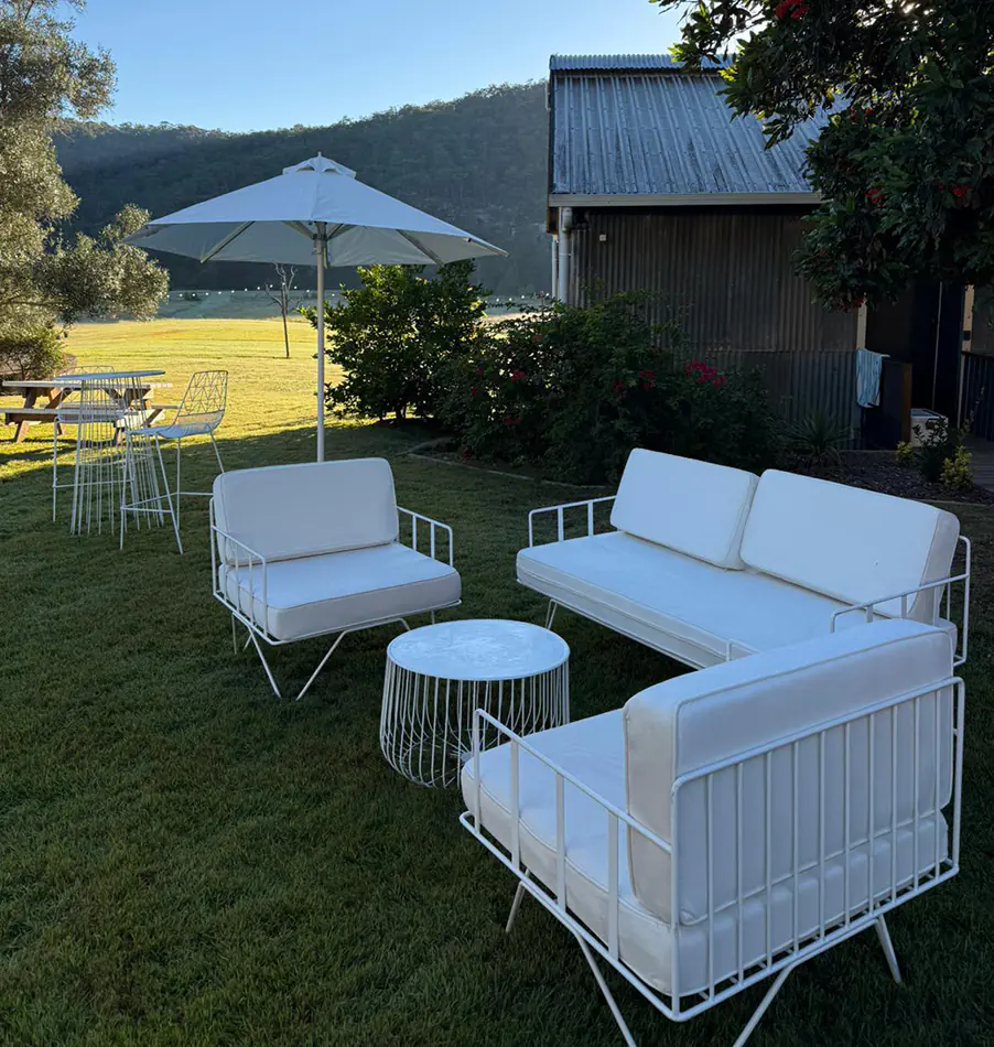White wire lounge seating with matching cushions and round wire coffee table positioned on a country event lawn beside outdoor umbrellas and rustic buildings