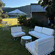 White wire lounge seating with matching cushions and round wire coffee table positioned on a country event lawn beside outdoor umbrellas and rustic buildings