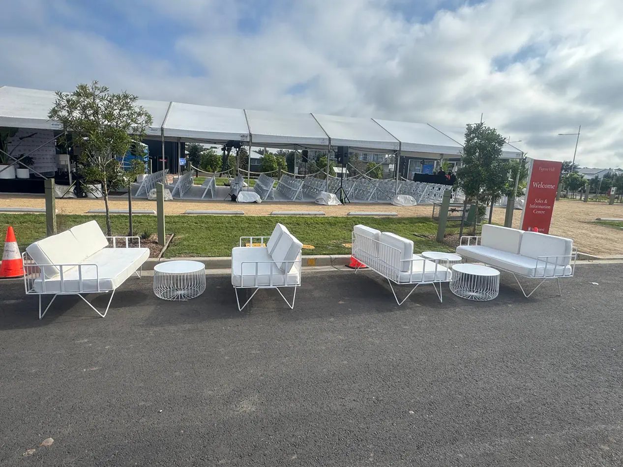 White wire lounge furniture with matching coffee tables arranged outside a large event marquee and ceremony seating setup