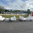 White wire lounge furniture with matching coffee tables arranged outside a large event marquee and ceremony seating setup