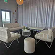 White wire lounge furniture with velvet cushions, round wire coffee table and ottoman stools styled inside a wedding and cocktail reception venue with white draped backdrop