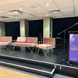 A stage set up with chairs and a podium, adorned with pink velvet cushions.