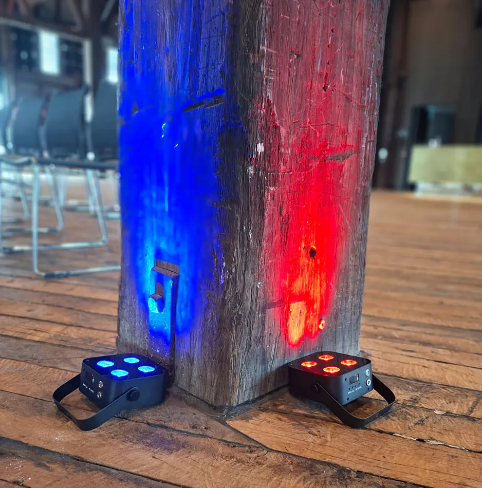 Wireless LED uplights creating blue and red lighting effects against a rustic timber post inside an event venue