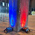 Wireless LED uplights creating blue and red lighting effects against a rustic timber post inside an event venue