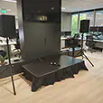 Wireless PA system with stage platform, twin speakers, microphones and large presentation screen setup inside a modern office event space