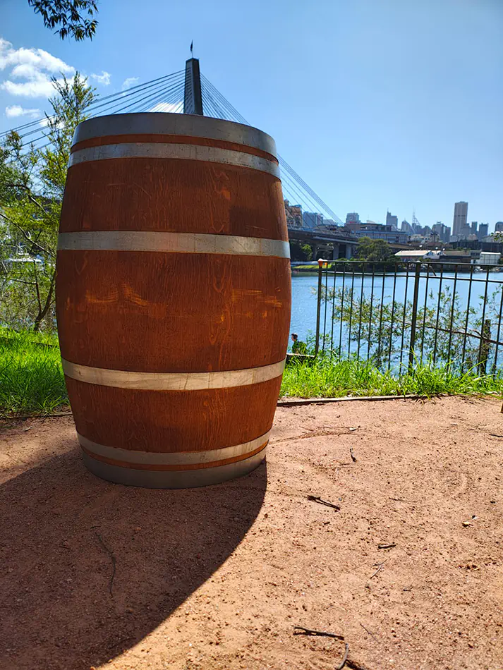 Wooden wine barrel styled as a cocktail table positioned outdoors near a river with city skyline and bridge in the background