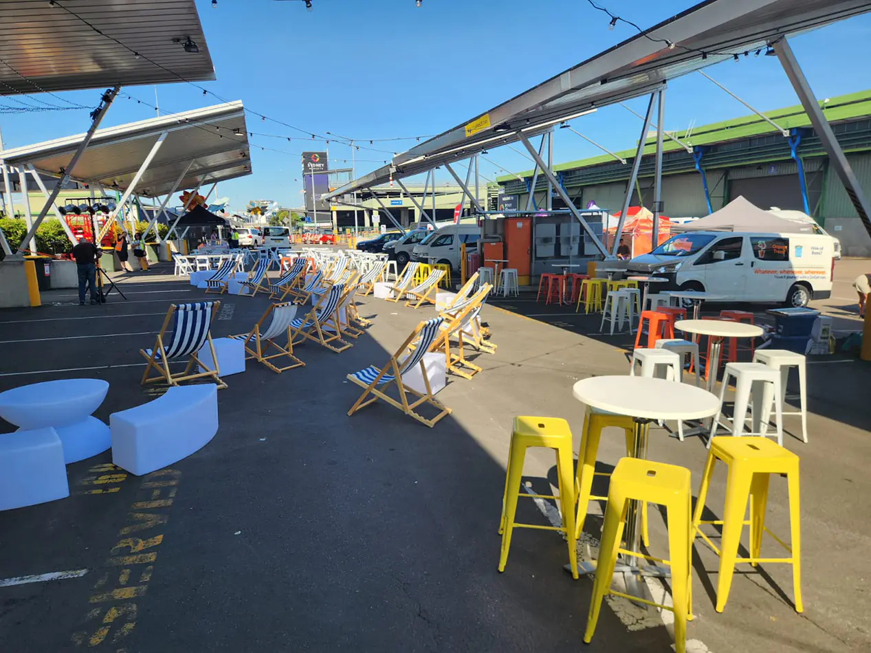 Yellow Tolix stools arranged around high tables in an outdoor event space with bar seating and market-style setup