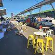 Yellow Tolix stools arranged around high tables in an outdoor event space with bar seating and market-style setup
