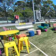 Yellow wire cocktail tables paired with stools in an outdoor lounge event setup with artificial grass, seating pods, and decorative elements