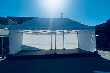 Covered stage platform beneath a white marquee with side walls, black skirting and open front access for an outdoor event setup