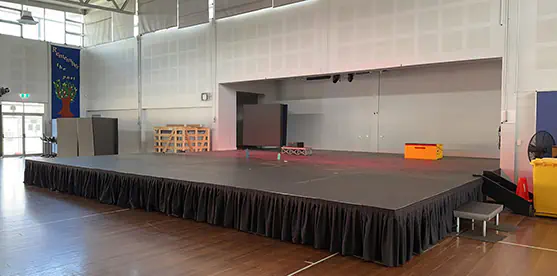 Large stage extension hire setup with black skirting, access step and wide modular platform added to an existing school hall stage