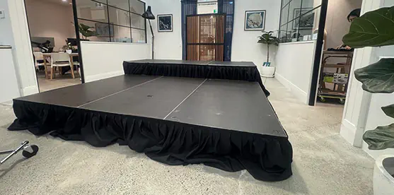 Modular black stage platform setup with skirted staging in a bright indoor venue with high ceilings, polished concrete flooring and a smaller rear platform