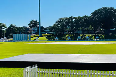 Outdoor stage hire platform set on a sports field with black skirting, open grass surrounds and white picket fencing in the foreground