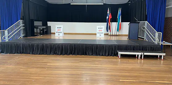 School hall stage extension with black skirting, timber flooring, side access step and a large modular platform extending the usable stage area