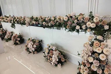 White bridal stage with blush and cream floral arrangements, greenery, glossy floor tiles and decorative wall panelling for an elegant wedding reception